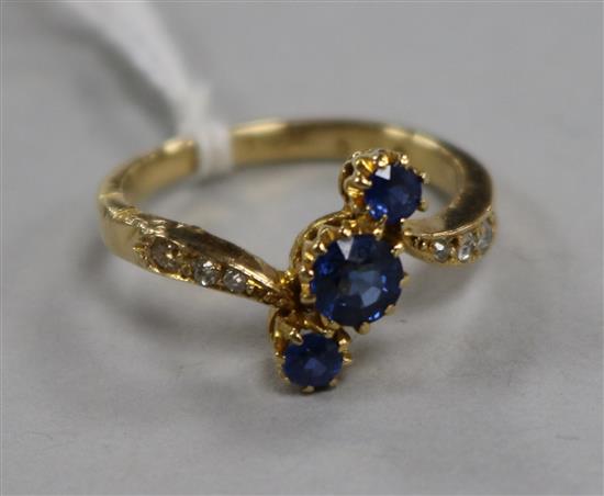 An 18ct gold and three stone sapphire crossover ring with diamond set shoulders, size L.